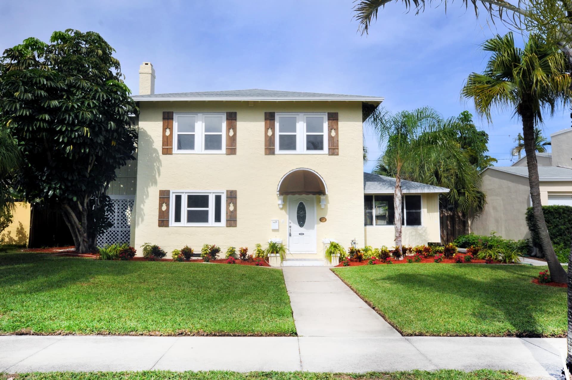 Pale yellow two-story home with walnut pineapple-cutout shutters framing every window