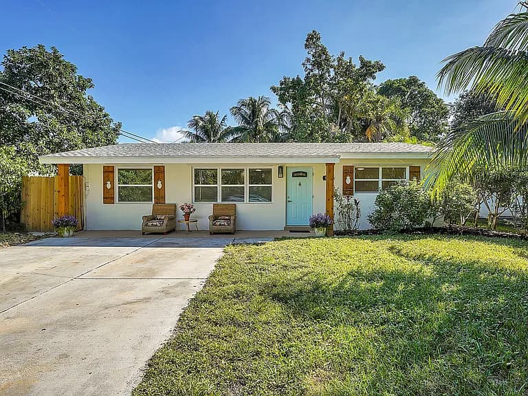 White home with dark wood shutters and a palm-lined yard