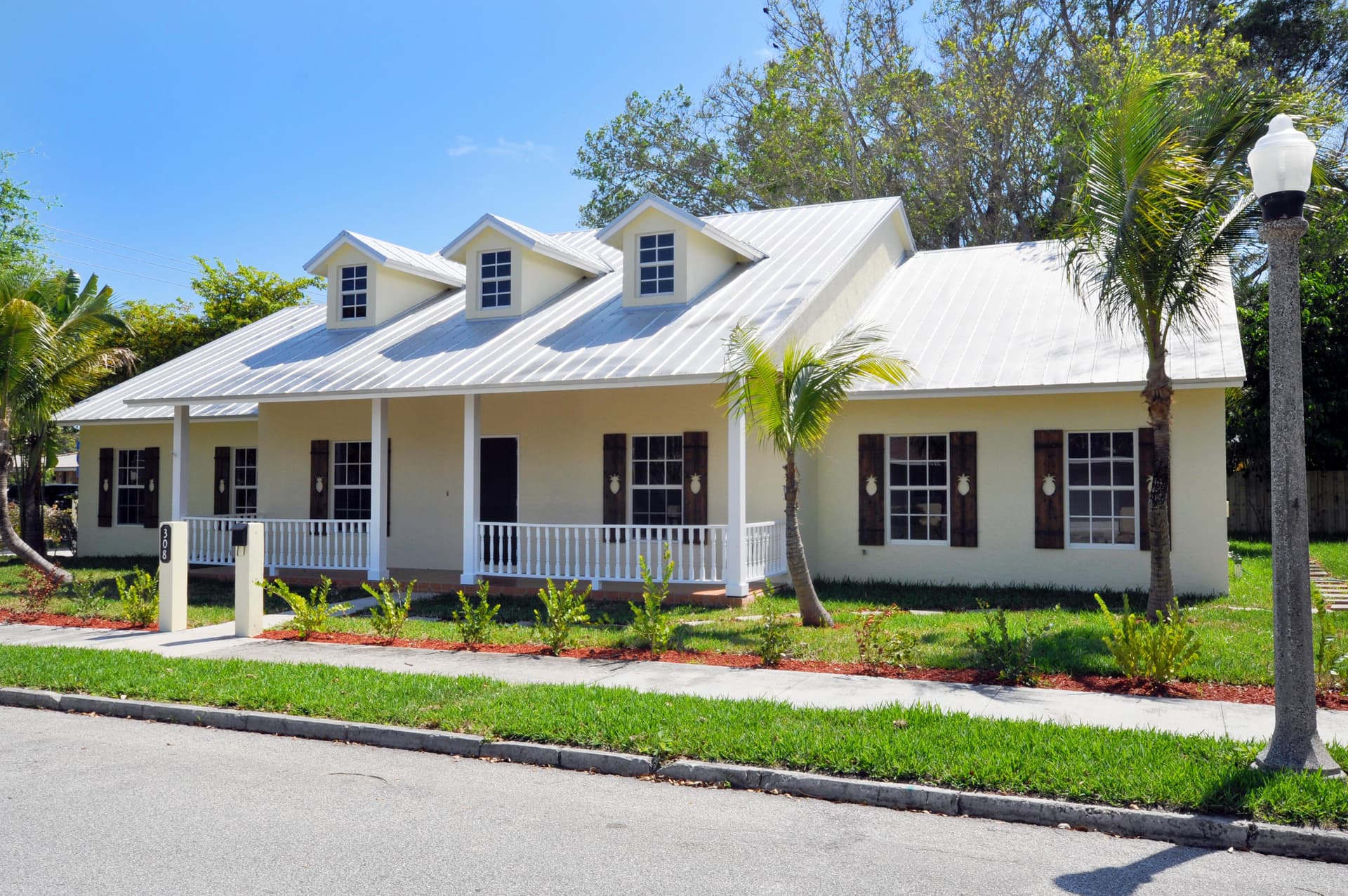Pale yellow ranch home with a standing-seam metal roof, triple dormers, and dark walnut pineapple-cutout shutters