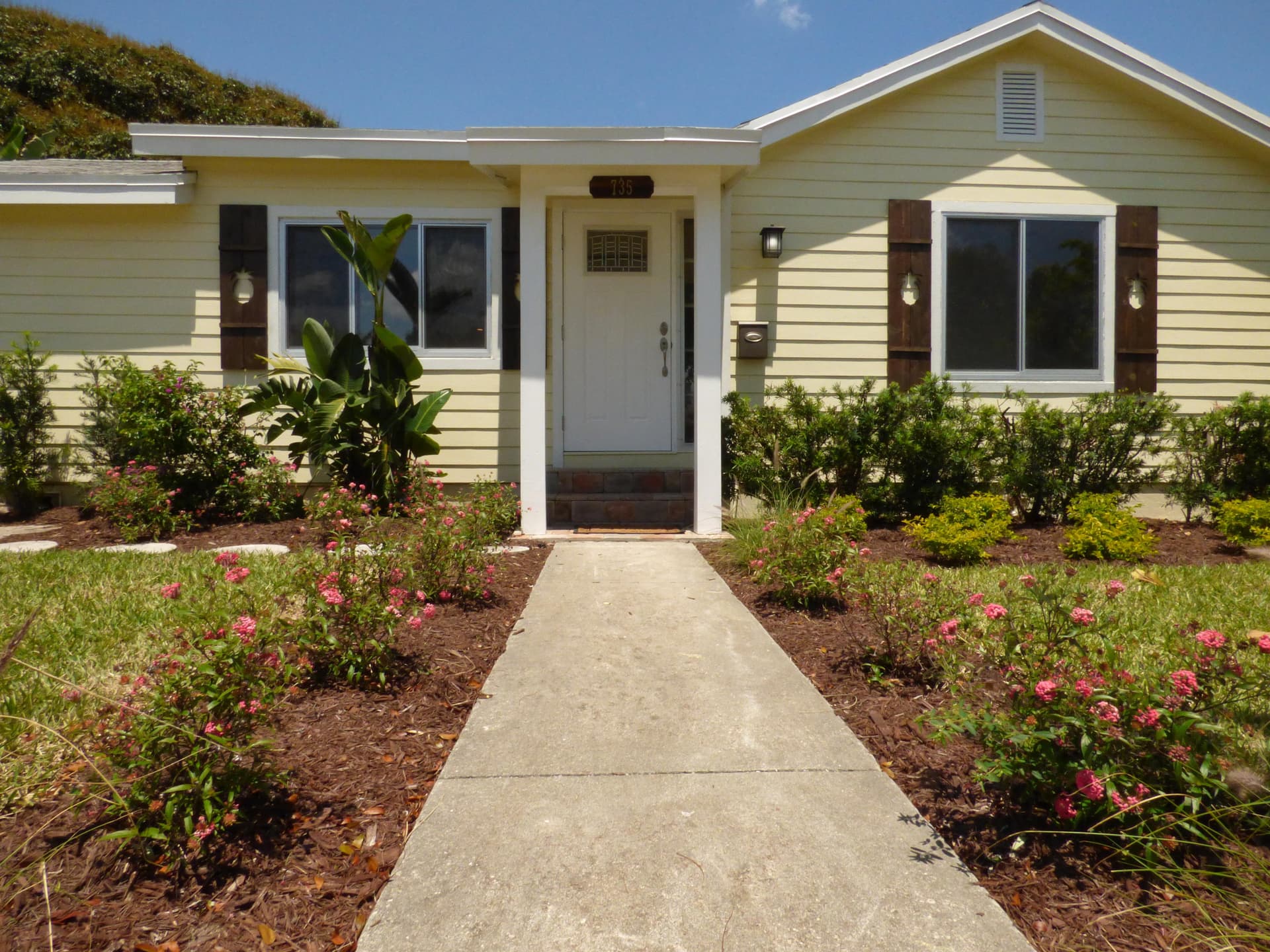 Pale yellow ranch home with a covered entry and dark walnut pineapple-cutout shutters